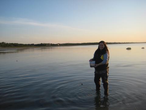 Lareen wading in water with bucket in hand at sunset